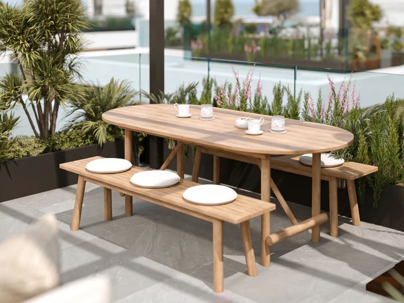 Wooden table and benches with white cushions on a planted terrace in golden light